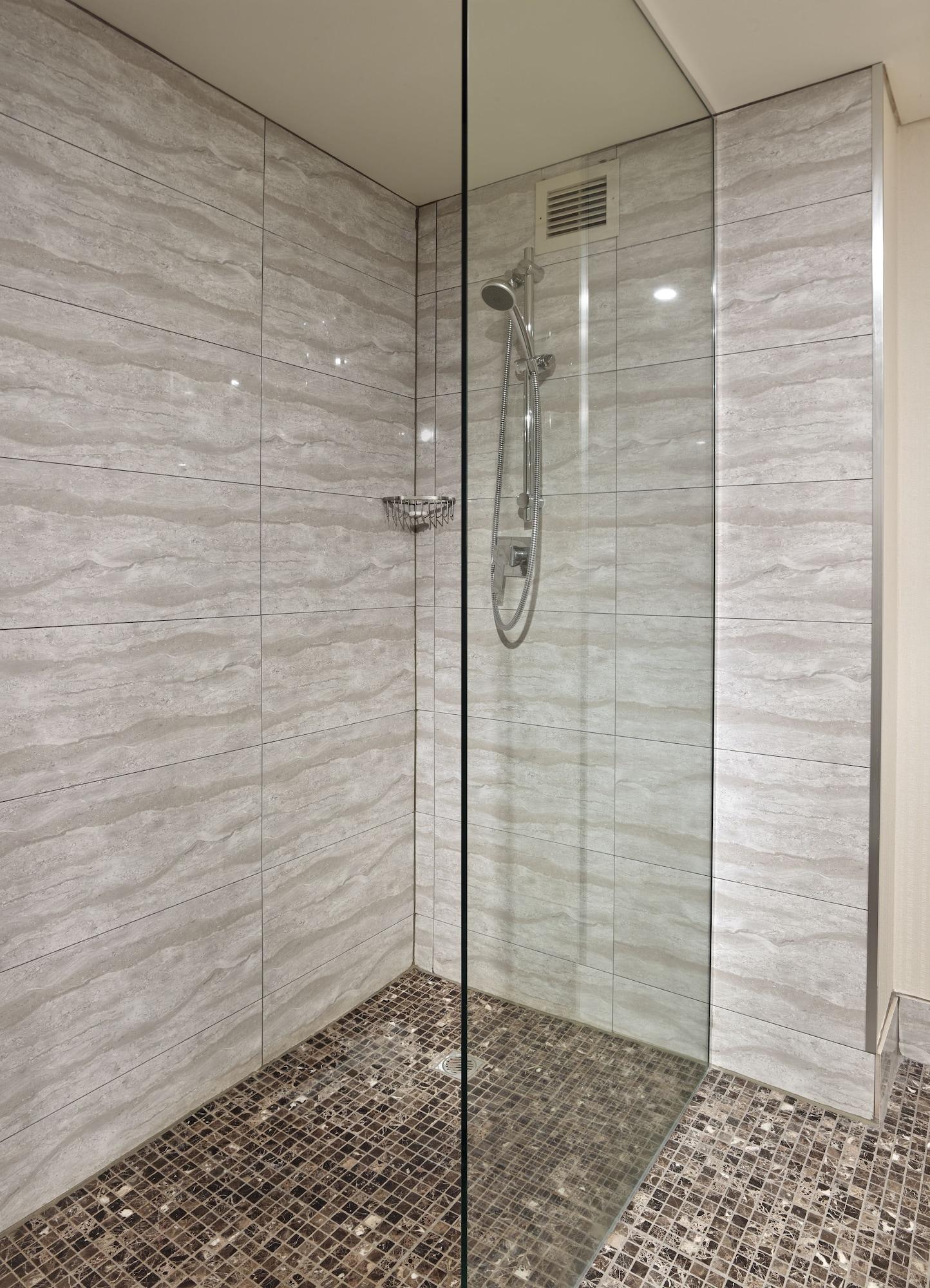 Отель Stamford Grand Adelaide Гленелг Экстерьер фото The photo shows a modern shower enclosure with a transparent glass door. The interior features tiled walls in a light, marble-like pattern, creating a clean and sleek look. There is a showerhead mounted on the wall, and the floor appears to be tiled 