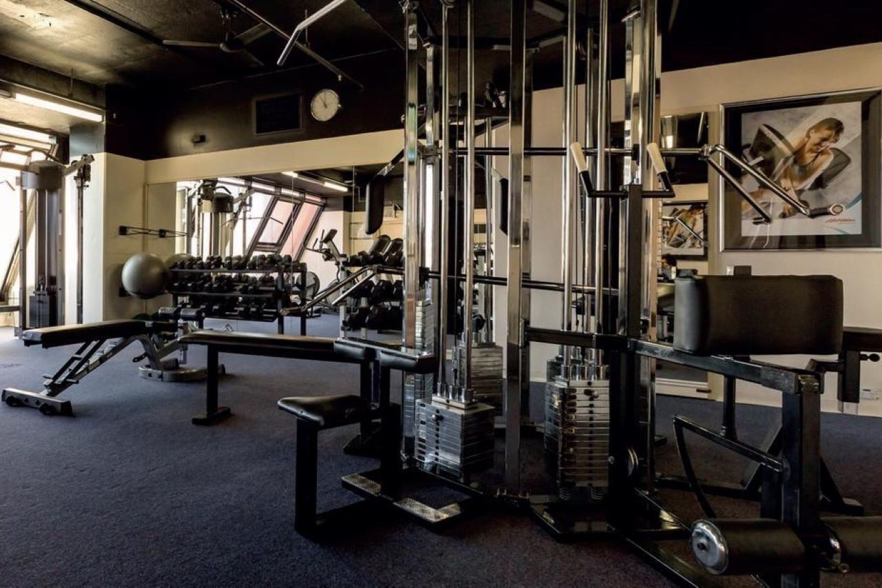 Отель Stamford Grand Adelaide Гленелг Экстерьер фото The photo shows a gym interior with various exercise equipment. In the foreground, there is a multi-station cable machine, which has several adjustable weights and pulleys for a variety of strength training exercises. To the side, there's a bench and